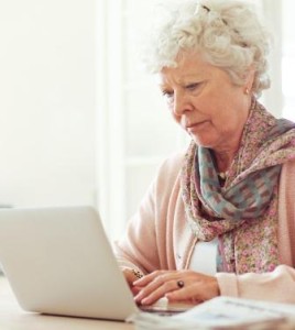Elderly woman at home typing something using her laptop